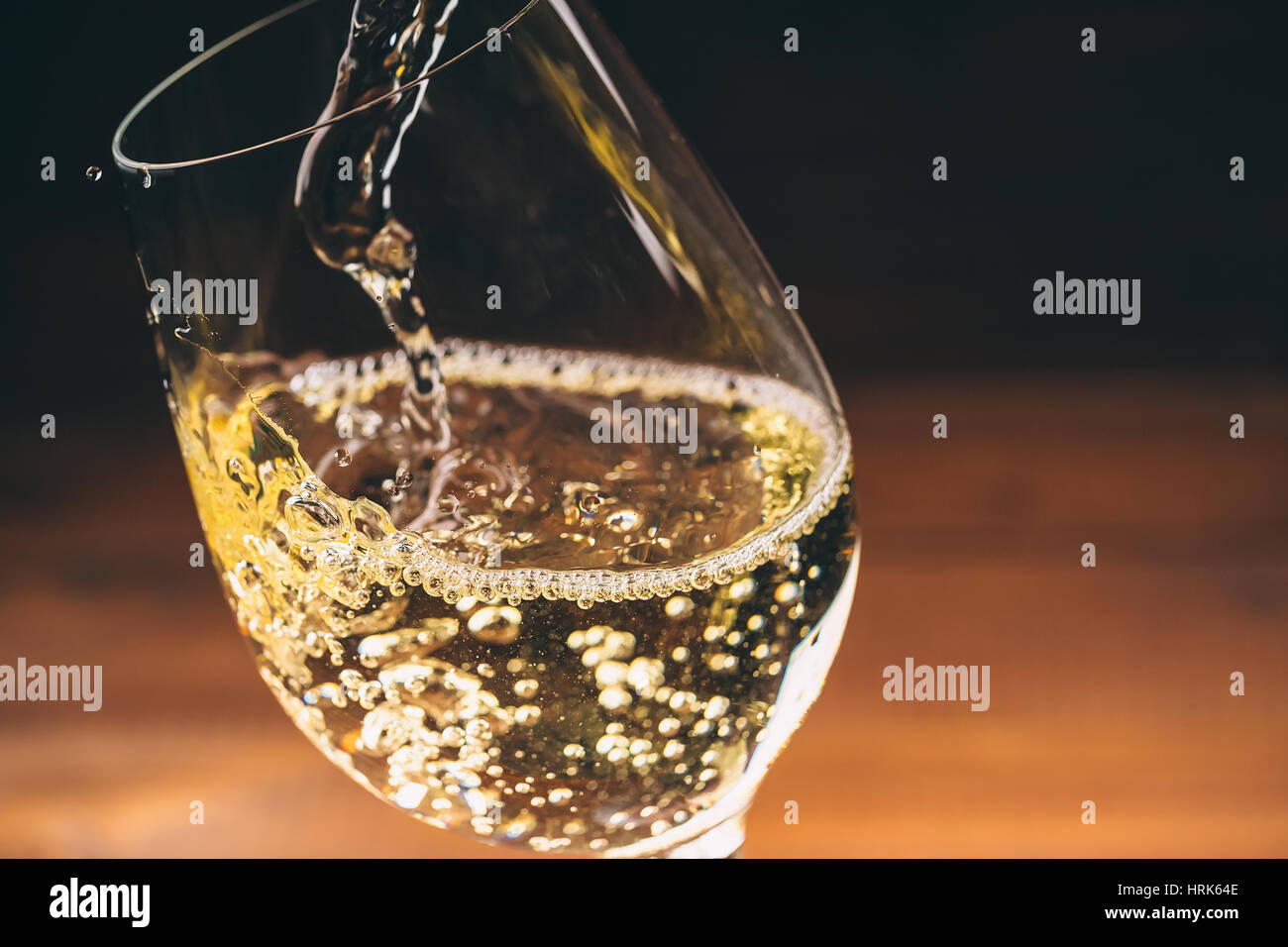 Versare il vino bianco da una bottiglia in un wineglasses su sfondo di legno. Spazio libero Foto Stock