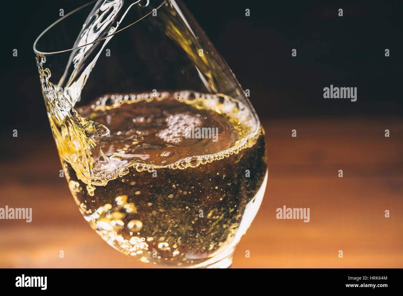 Versare il vino bianco da una bottiglia in una vista ravvicinata della wineglasses contro lo sfondo di legno Foto Stock