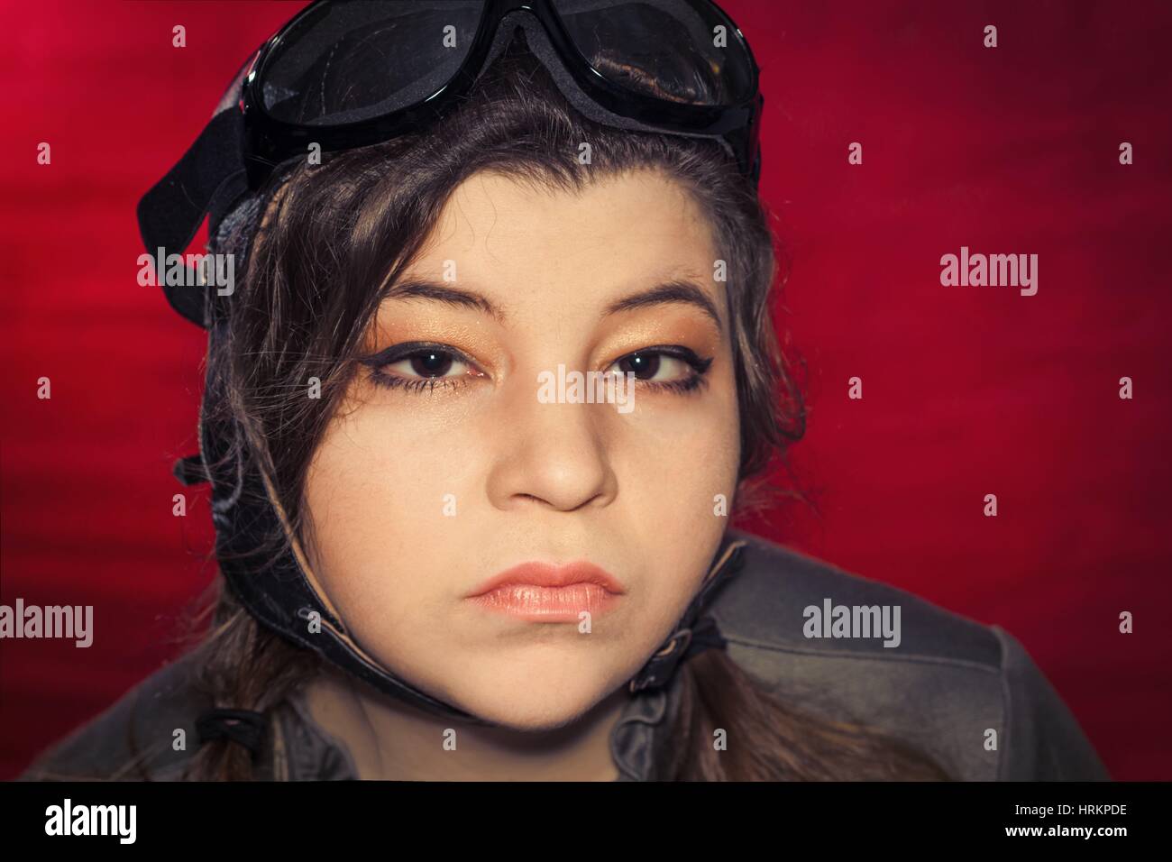 Ragazza indossando aviatore cappello e occhiali rende stupida espressione facciale dal forte vento Foto Stock