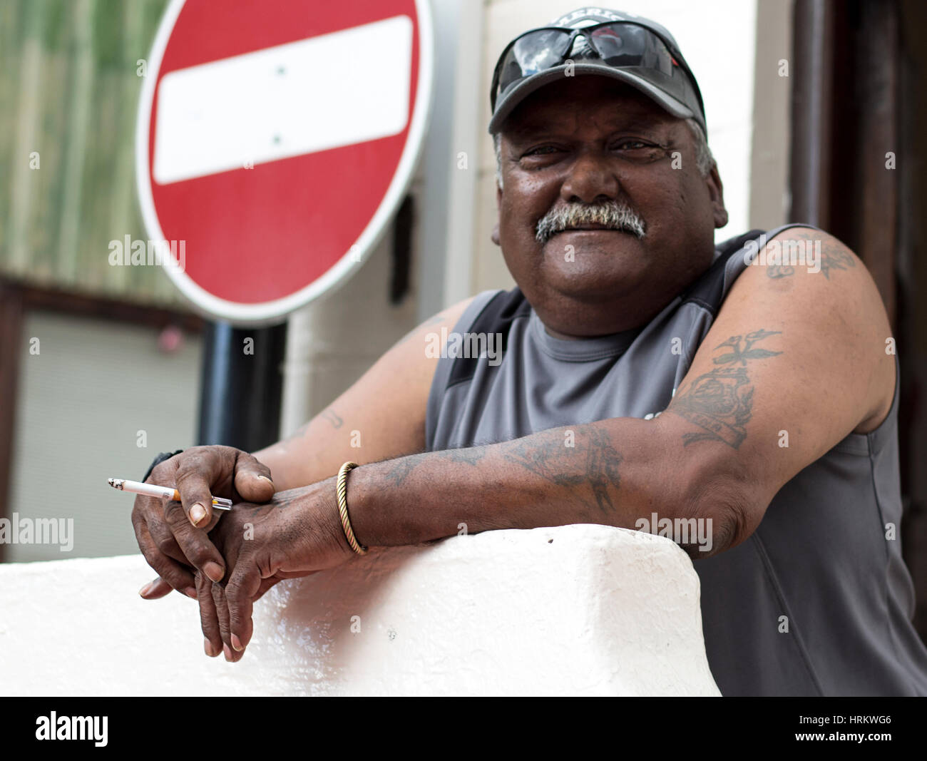 Uomo con i baffi tenendo una sigaretta. Un modo sbagliato di segno è dietro di lui. Foto Stock