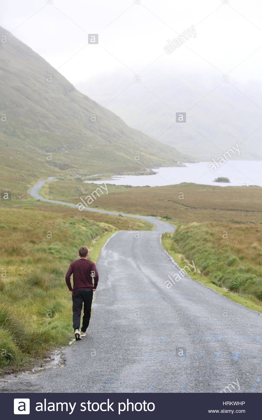 Un giovane uomo cammina la strada attraverso Doolough Valley in Mayo Irlanda nel suo viaggio attraverso il west. Foto Stock