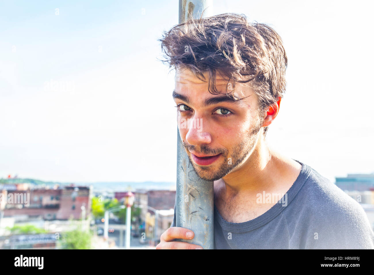 Un giovane uomo appoggiato in un polo di strada guardando direttamente nella fotocamera con sky e gli edifici dietro. Foto Stock