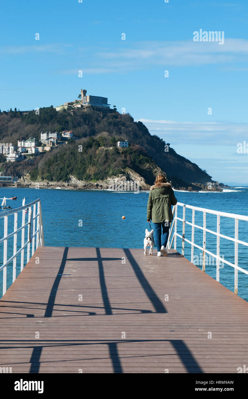 Spagna: la donna con un cane sul molo a Donostia-San Sebastian, con vista della spiaggia di La Concha, considerata una delle migliori spiagge della città in Europa Foto Stock