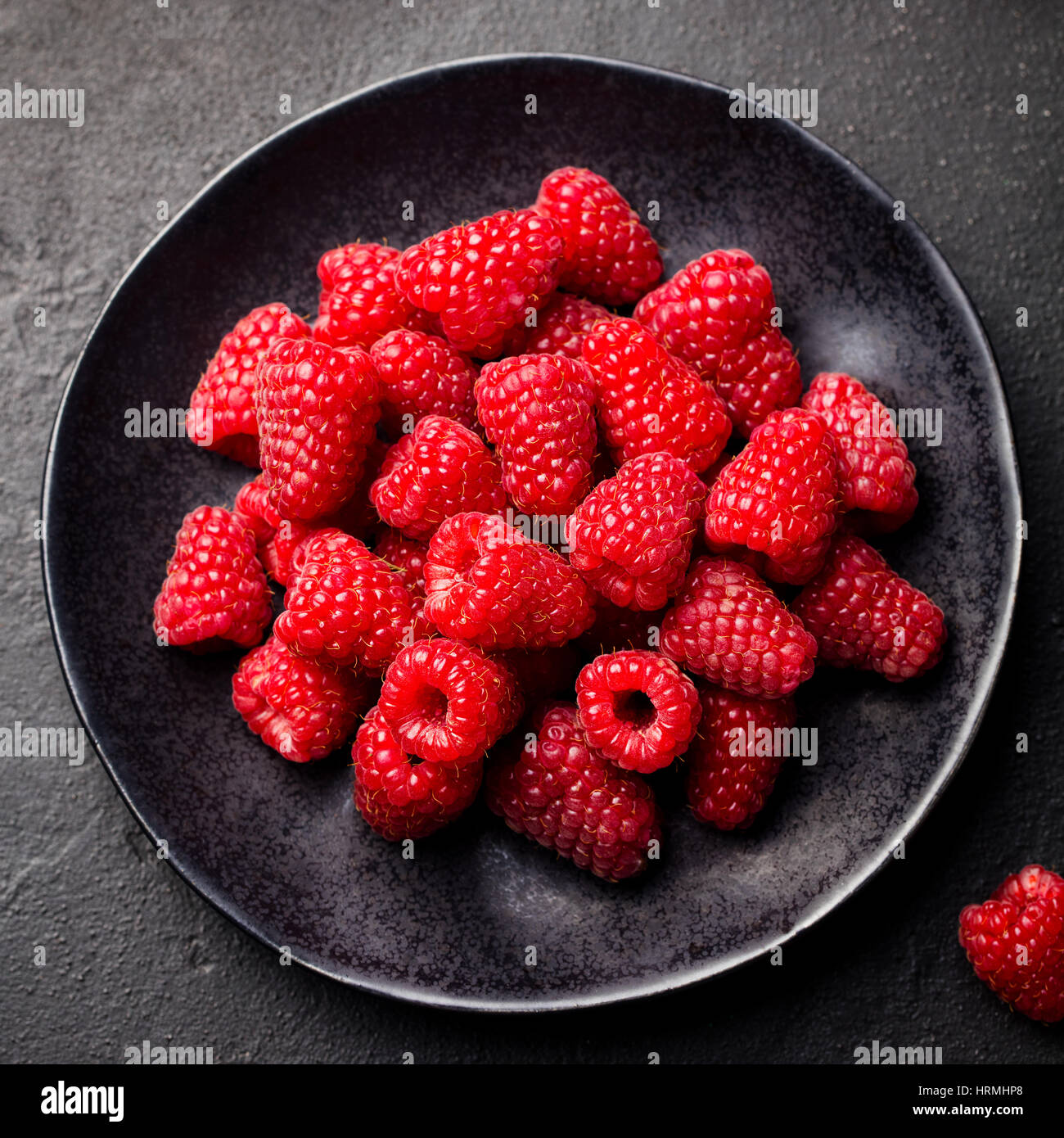 Lamponi freschi su una ciotola nero. Sfondo di ardesia vista dall'alto. Foto Stock