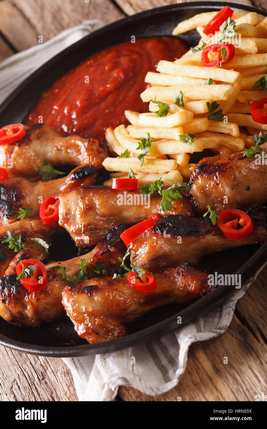 Ali di pollo piccanti con patatine fritte e ketchup su una piastra di close-up verticale. Foto Stock