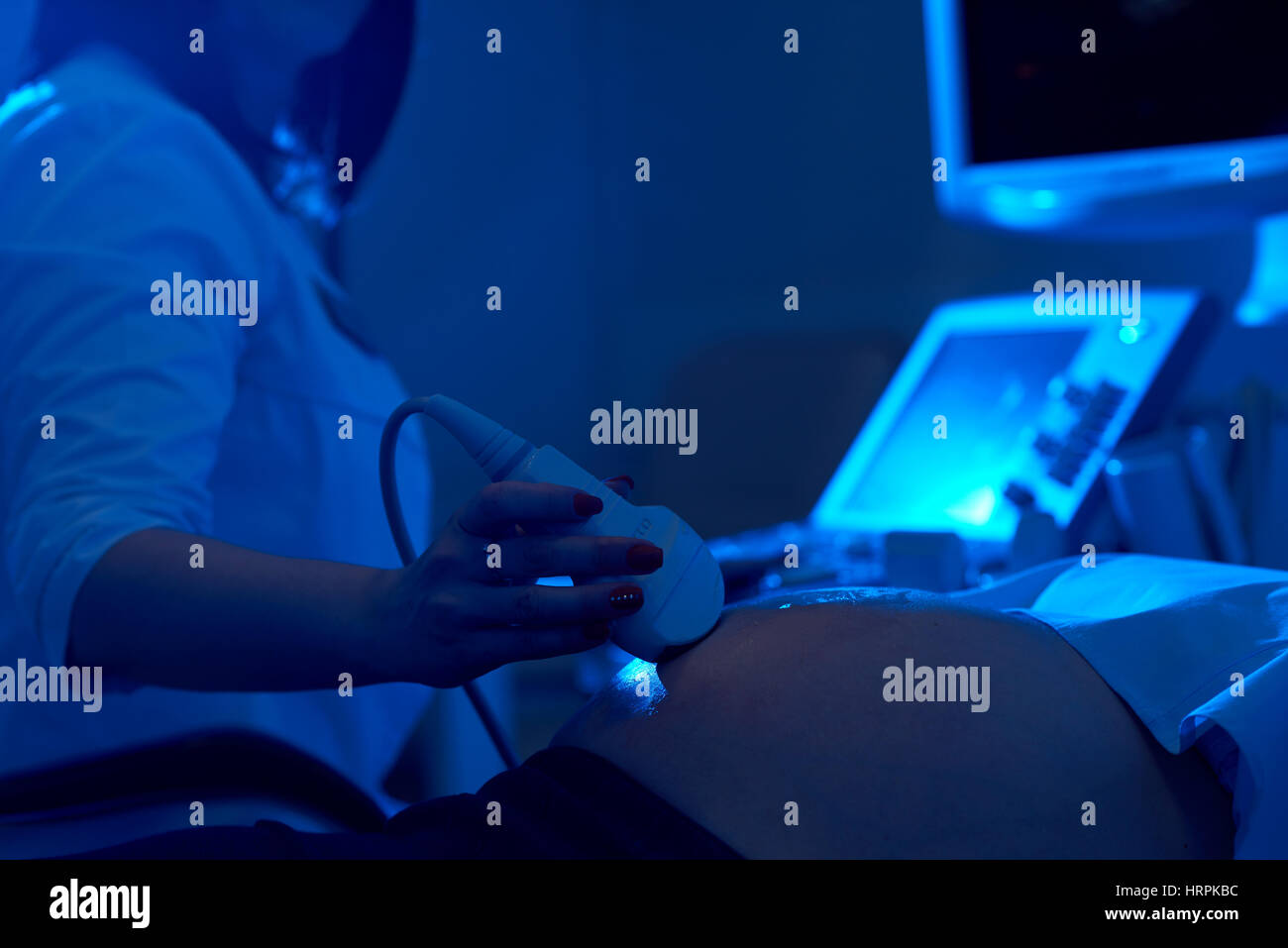 Raccolto di medico professionale utilizzando apparecchiature a ultrasuoni con gel lo screening di donna incinta al buio. Dottore in bianco uniforme di toccare lo stomaco del FEMA Foto Stock