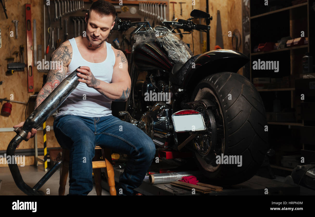 Pensare di aria pura. Bel uomo barbuto avente pensieri positivi seduto sulla sedia accanto alla moto mentre guardando lo sfiato di gas Foto Stock