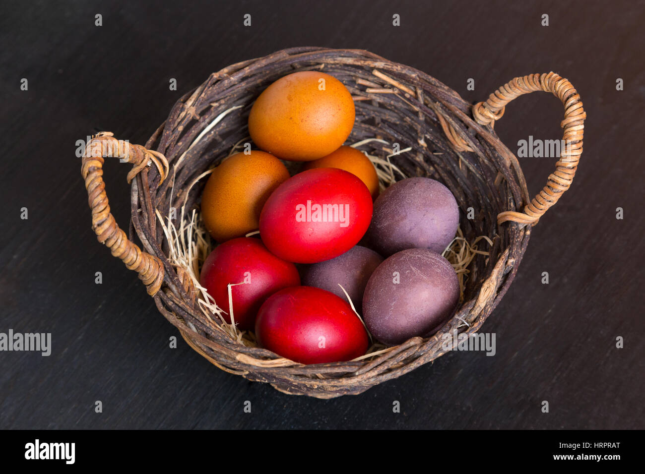 Cesto in Vimini con colorate uova di Pasqua sulla tavola di legno, primo piano Foto Stock