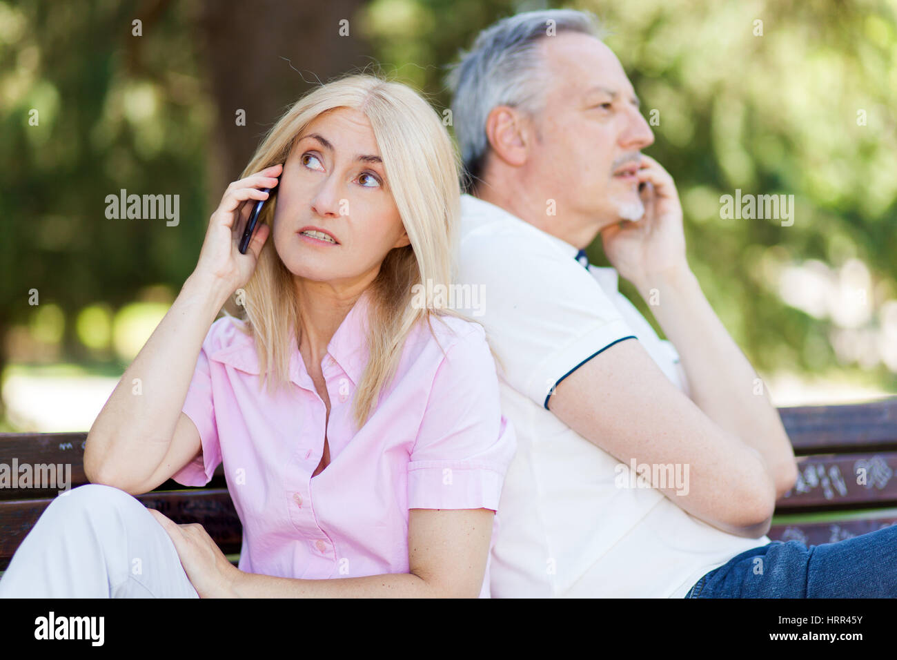 Coppia senior seduta di schiena parlando su telefoni cellulari Foto Stock
