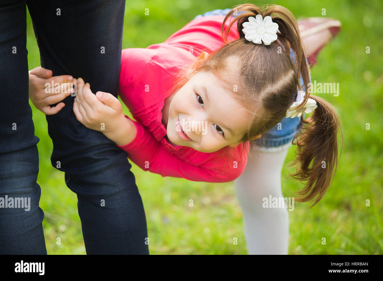 Closeup ritratto di famiglia felice su erba verde dello sfondo. Poco funny girl di 4 anni di età al di fuori a giocare con i suoi genitori in primavera il parco della città. H Foto Stock
