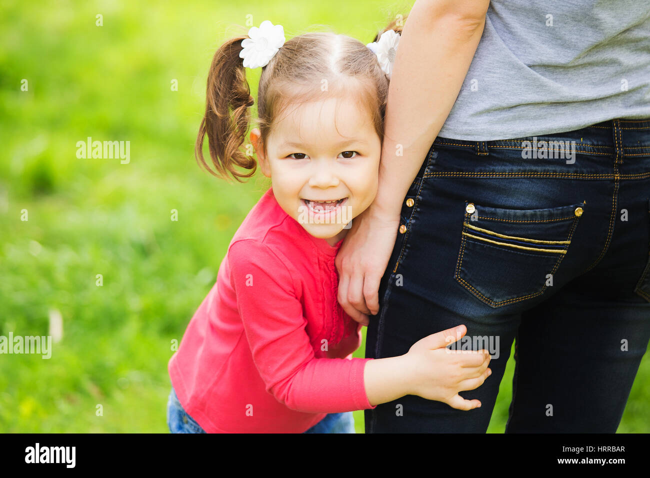 Closeup ritratto di famiglia felice. Poco funny girl di 4 anni di età al di fuori a giocare con i suoi genitori in primavera il parco della città. Baby abbraccia i fianchi della madre e Foto Stock