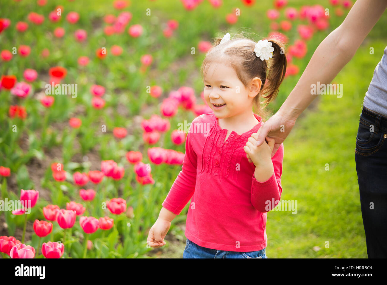 Closeup ritratto di famiglia felice. Poco funny girl di 4 anni età cammina lungo aiuola di tulipani tenendo la mano della mamma in primavera il parco della città. Horizont Foto Stock