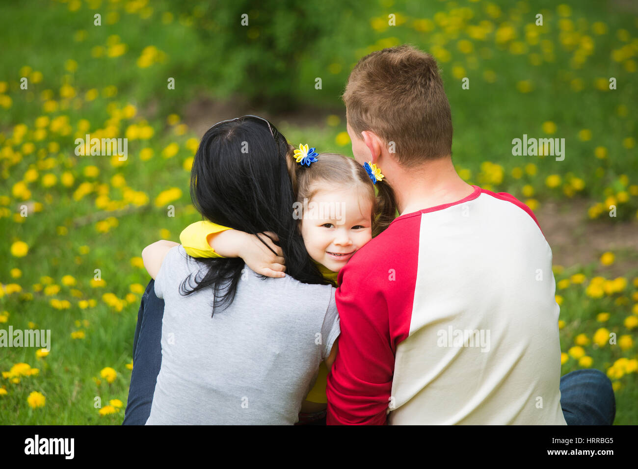 Closeup ritratto di famiglia felice. Poco funny girl di 4 anni di età al di fuori a giocare con i suoi genitori in primavera il parco della città. Orizzontale della fotografia a colori Foto Stock