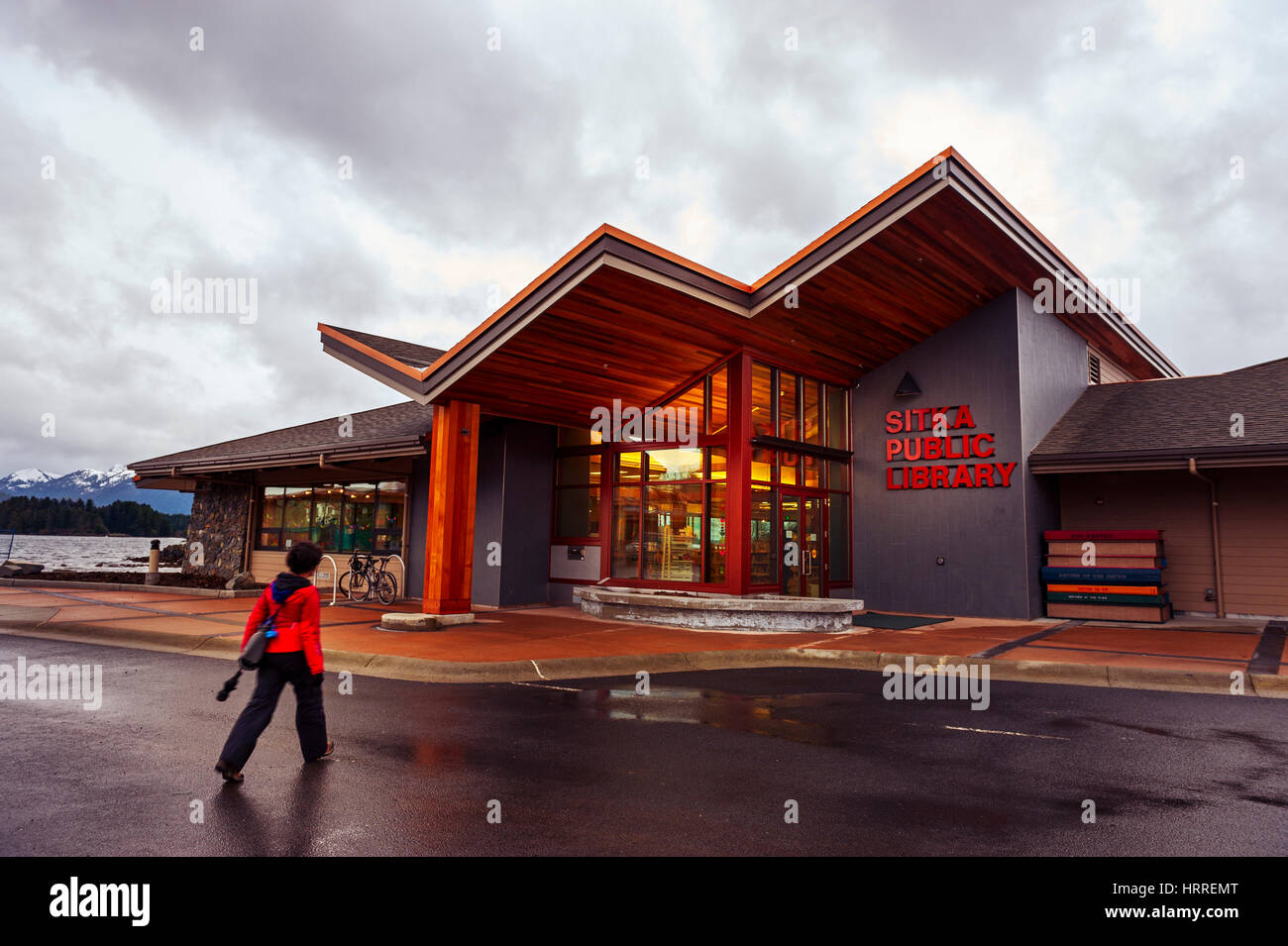 Donna in rosso Giacca pioggia a piedi da Sitka Biblioteca Pubblica nel centro cittadino di Sitka, Alaska, Stati Uniti d'America. Fotografia di Jeffrey Wickett, NorthLight fotografia. Foto Stock