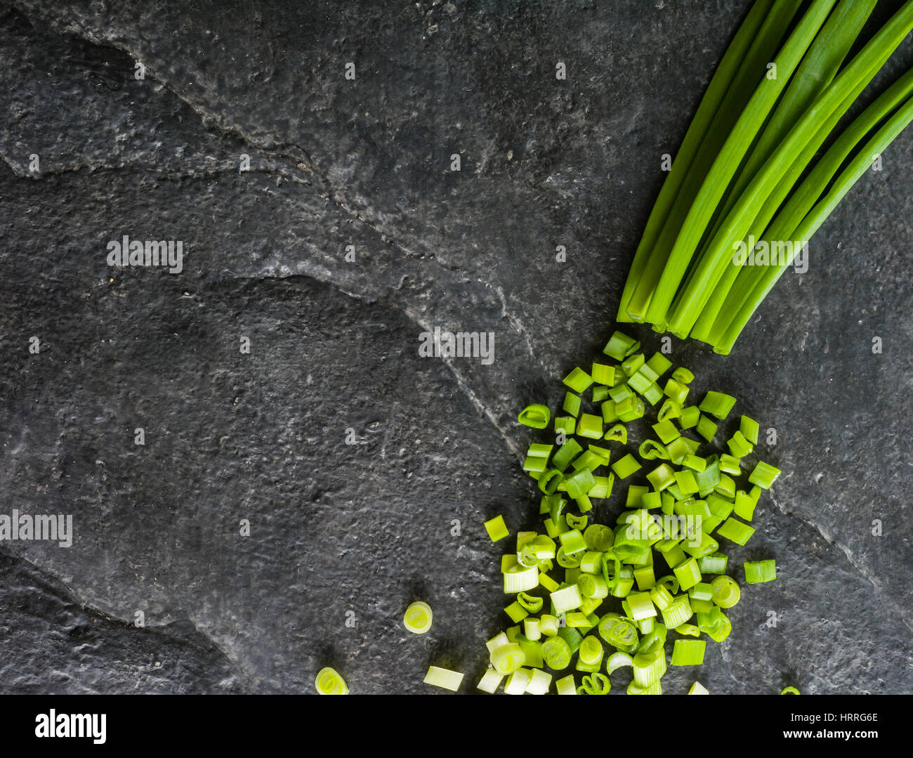 Il taglio del fascio di cipolle verdi su uno sfondo di nero ardesia. Spazio per il testo. Vista da sopra. Foto Stock