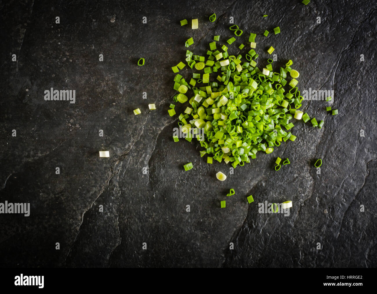 Il taglio del fascio di cipolle verdi su uno sfondo di nero ardesia. Spazio per il testo. Vista da sopra. Foto Stock