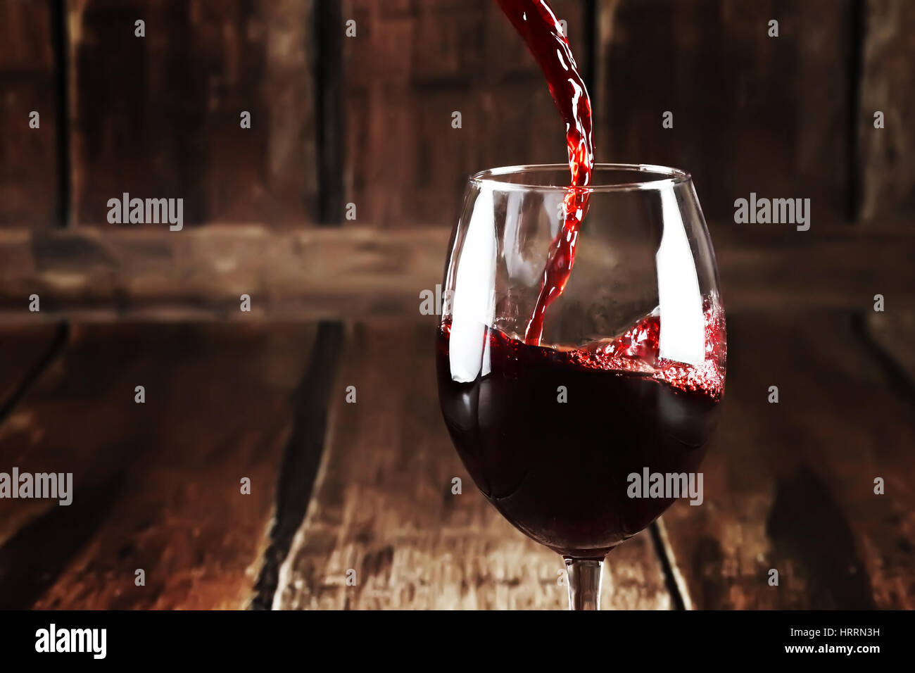 Primo piano di vetro con un bicchiere di vino rosso su sfondo di legno. Close up versando il vino in vetro trasparente. Perfetto sfondo alcolica. Macro di vino rosso Foto Stock