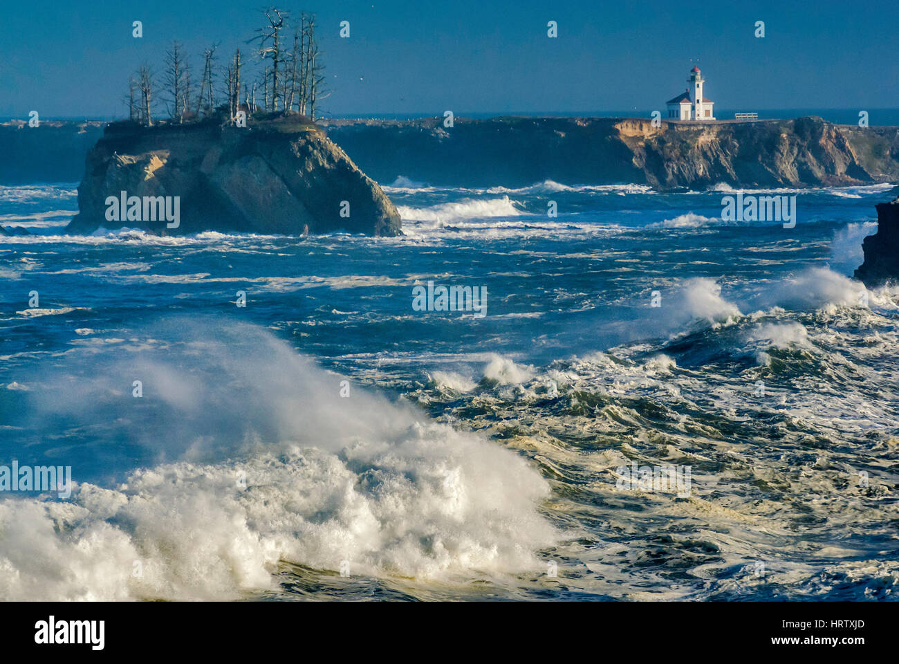 Onde enormi e laminazione di schiantarsi al tramonto Cove, Cape Arago faro in distanza, vicino a Charleston, Oregon, Stati Uniti d'America Foto Stock