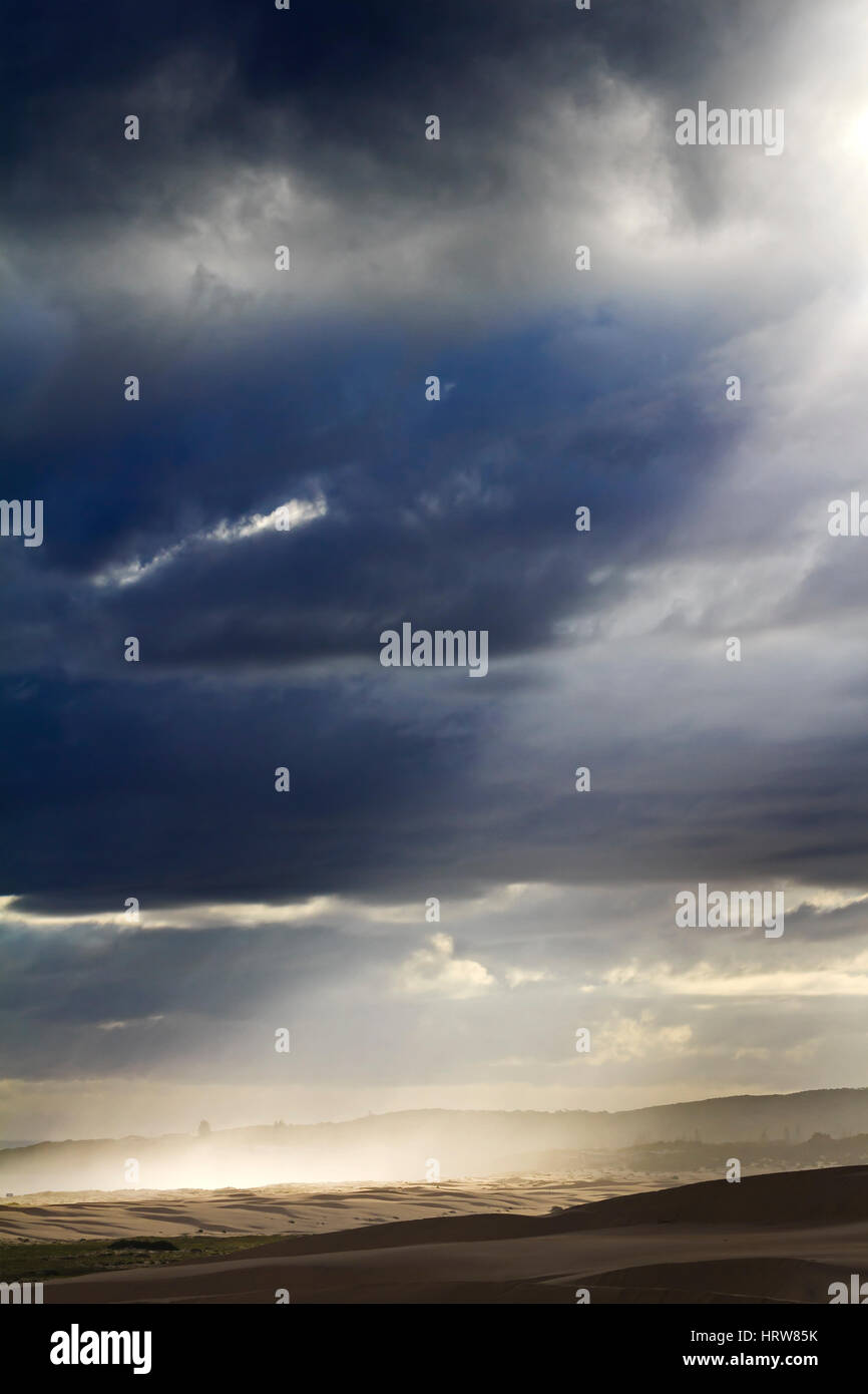 Raggio luminoso della luce tramite thick Dark nuvole temporalesche su costo australiano e le dune di sabbia come una fusione di aria, acqua e terra di elementi. Foto Stock