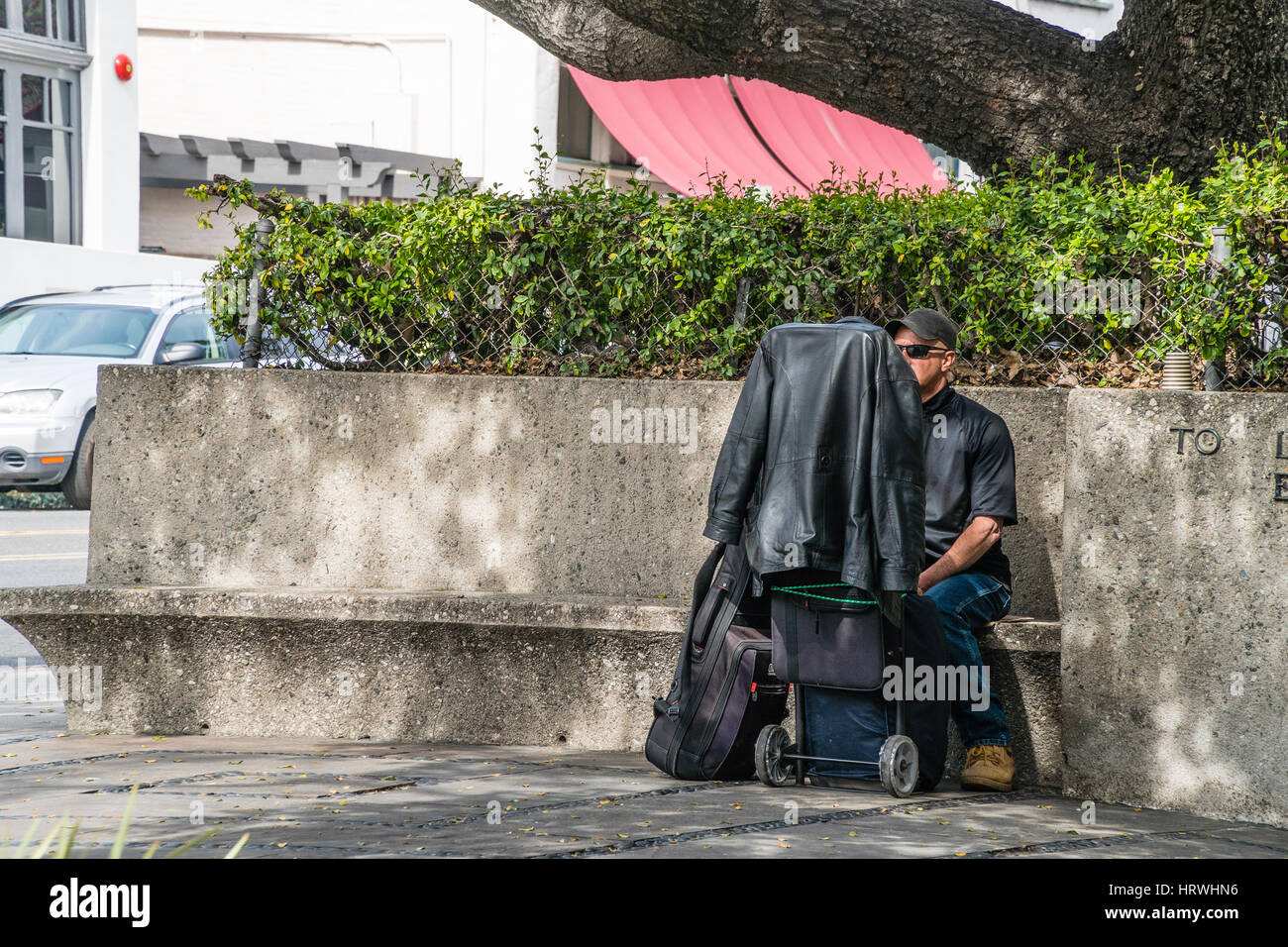 Senzatetto uomo vestito di nero seduta con il suo bagaglio su un banco di  cemento a Santa Barbara, CA Foto stock - Alamy