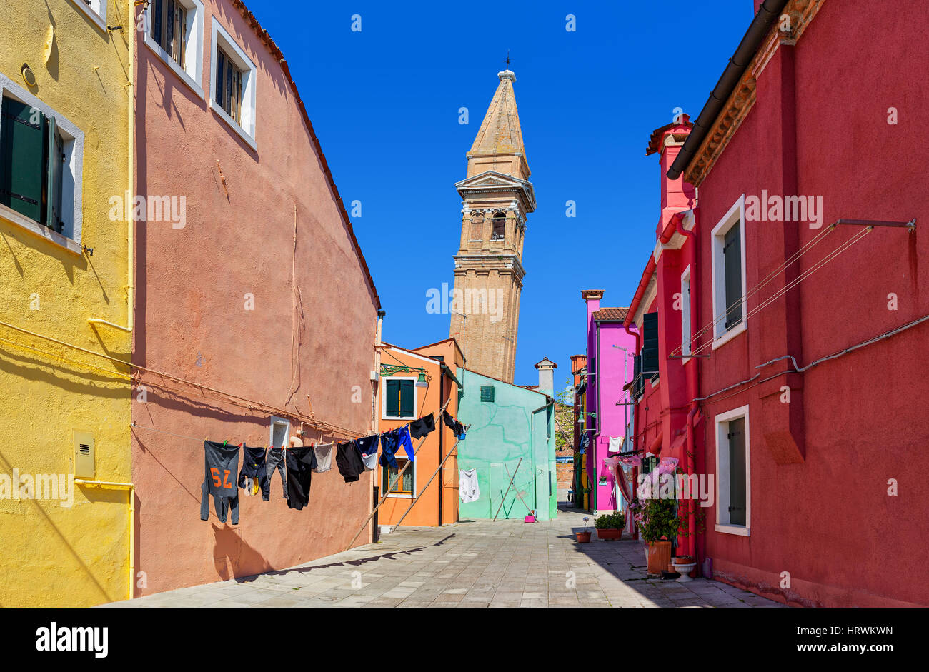 Piccolo cortile tra case colorate e la torre campanaria inclinata su sfondo sotto il cielo blu sull isola di Burano, Italia. Foto Stock
