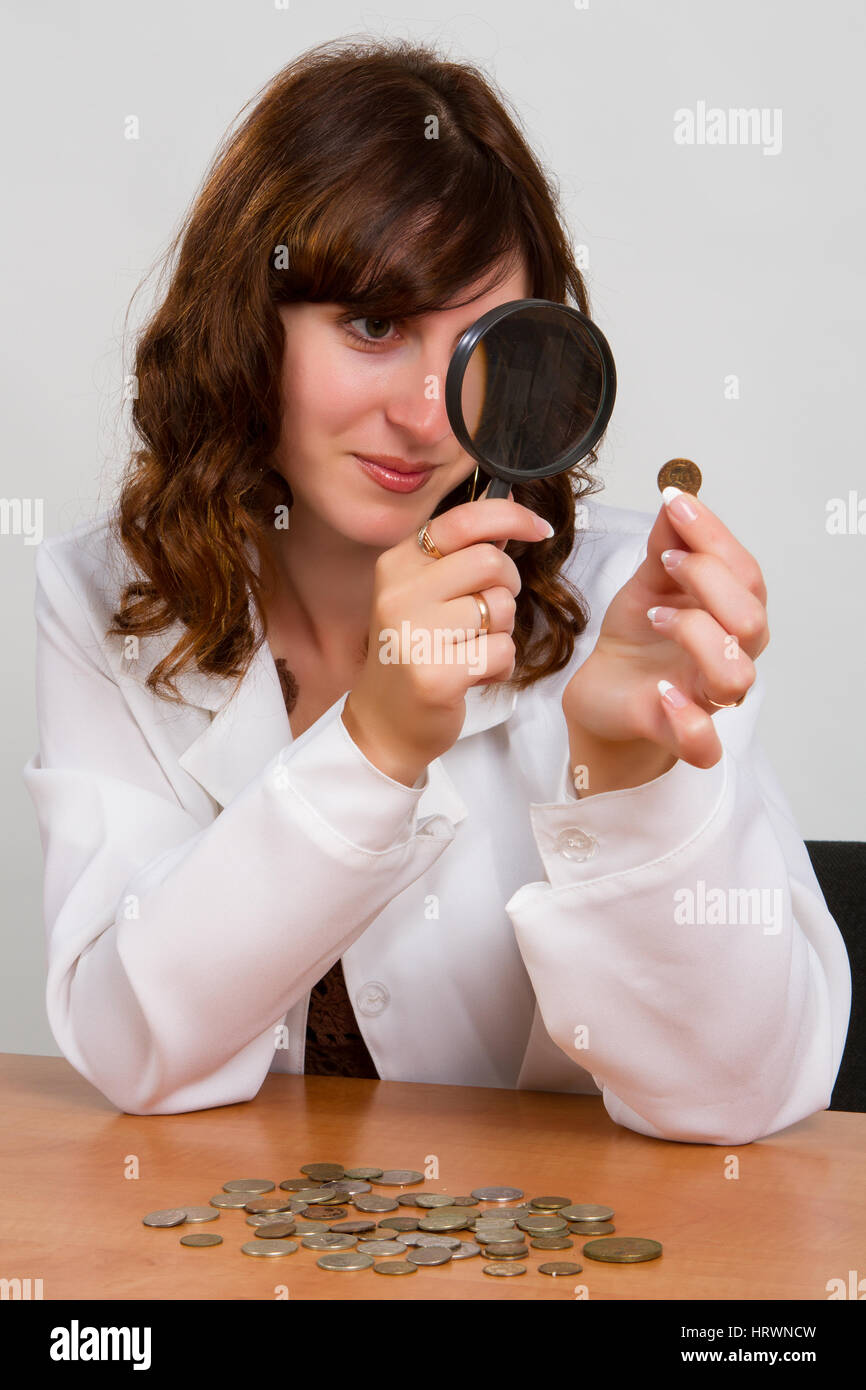 Concetto finanziario, tenere in mano la lente di ingrandimento e delle monete metalliche in euro Foto Stock