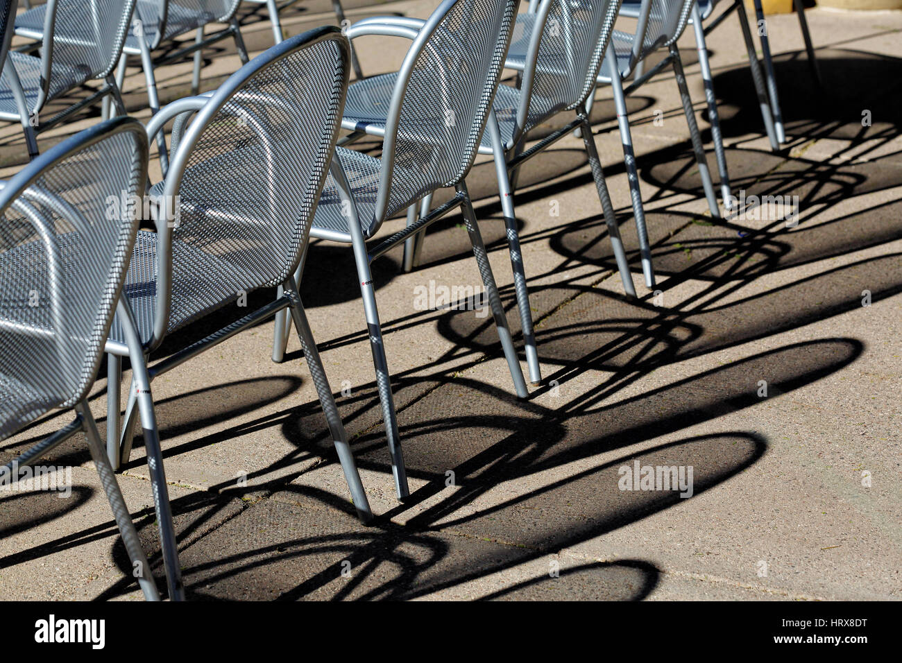Il modello shadow su calcestruzzo, causata dal basso angolo la luce del sole che splende attraverso maglie di metallo sedie. Foto Stock