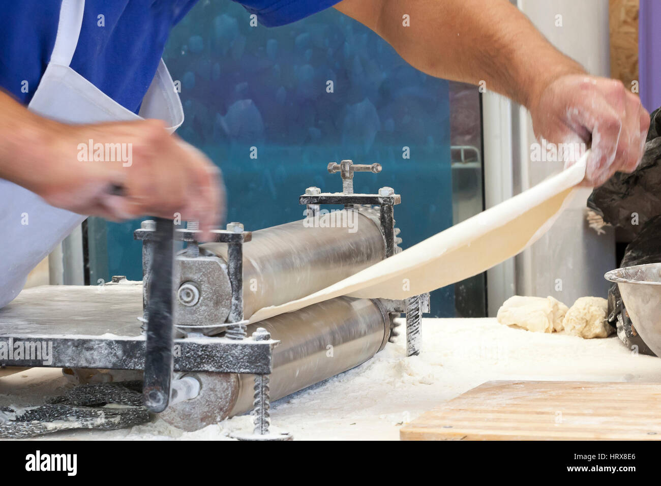 Gli uomini le mani stendere l'impasto da vicino. L'uomo la preparazione di impasti per la cottura della pasta su una tavola di legno in cafe Foto Stock