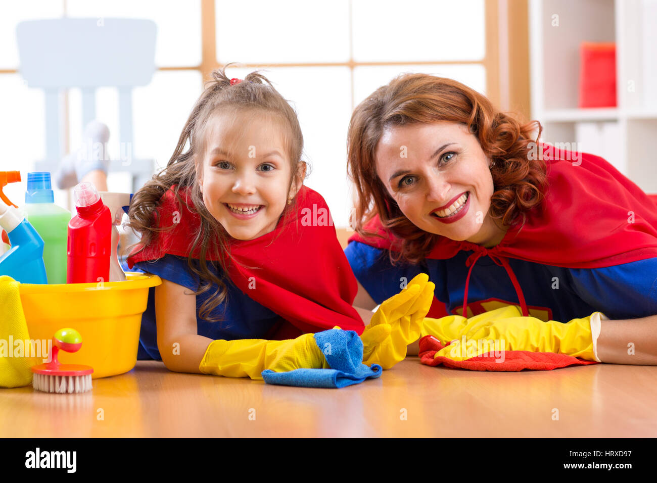 Carino donna e di sua figlia bambini vestiti da supereroi la pulizia del pavimento e sorridente Foto Stock