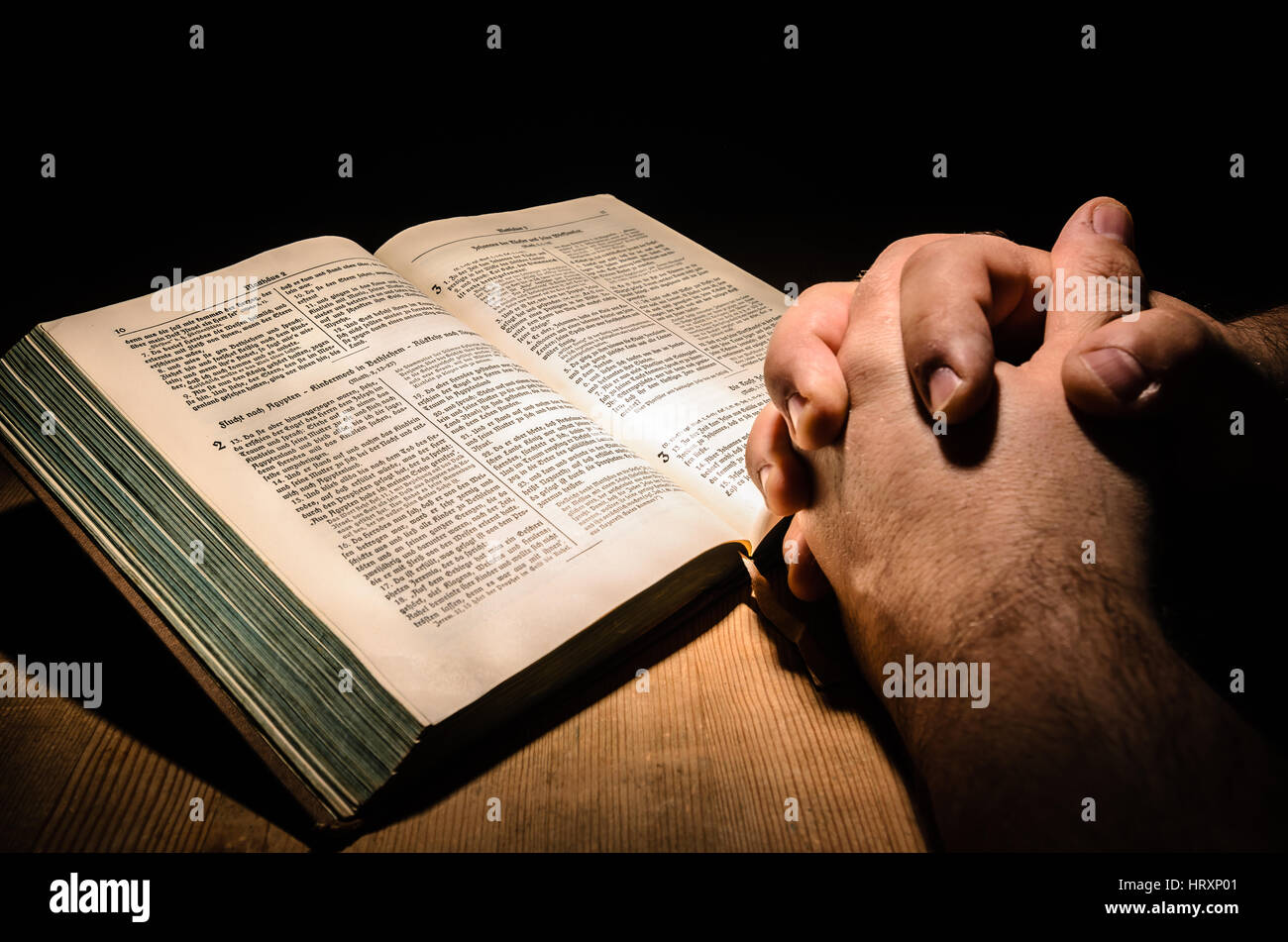 Le mani collocate su una bibbia, tavolo in legno con sfondo scuro Foto Stock