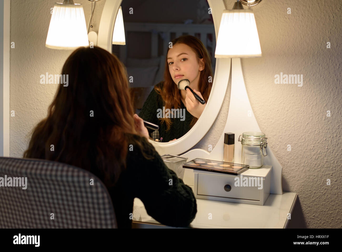 Giovane donna l'applicazione di cosmetici per il trucco di fronte a uno specchio a casa Foto Stock