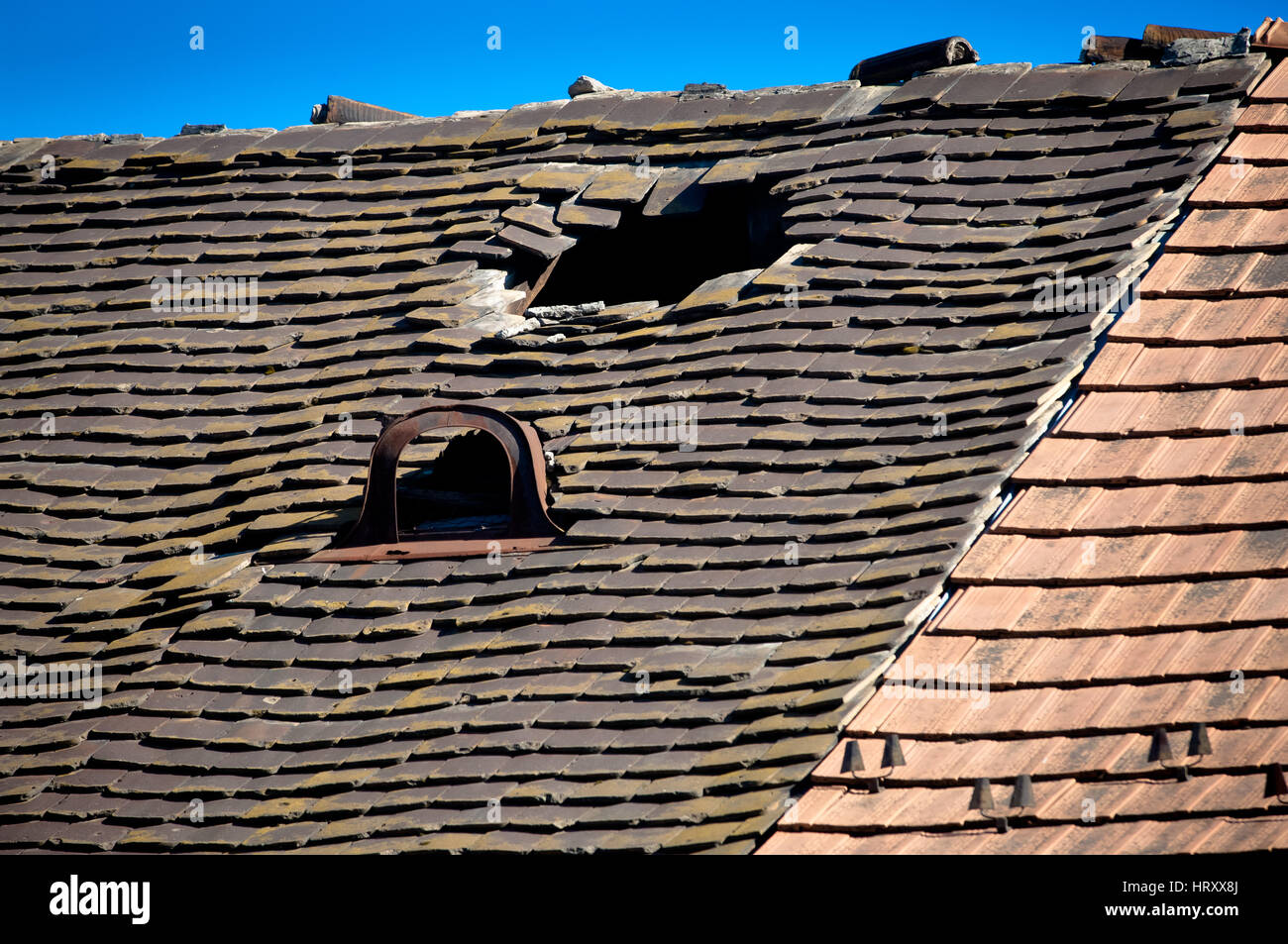 Vecchio danneggiato tetto di tegole con piastrelle rotte e un foro sul tetto Foto Stock