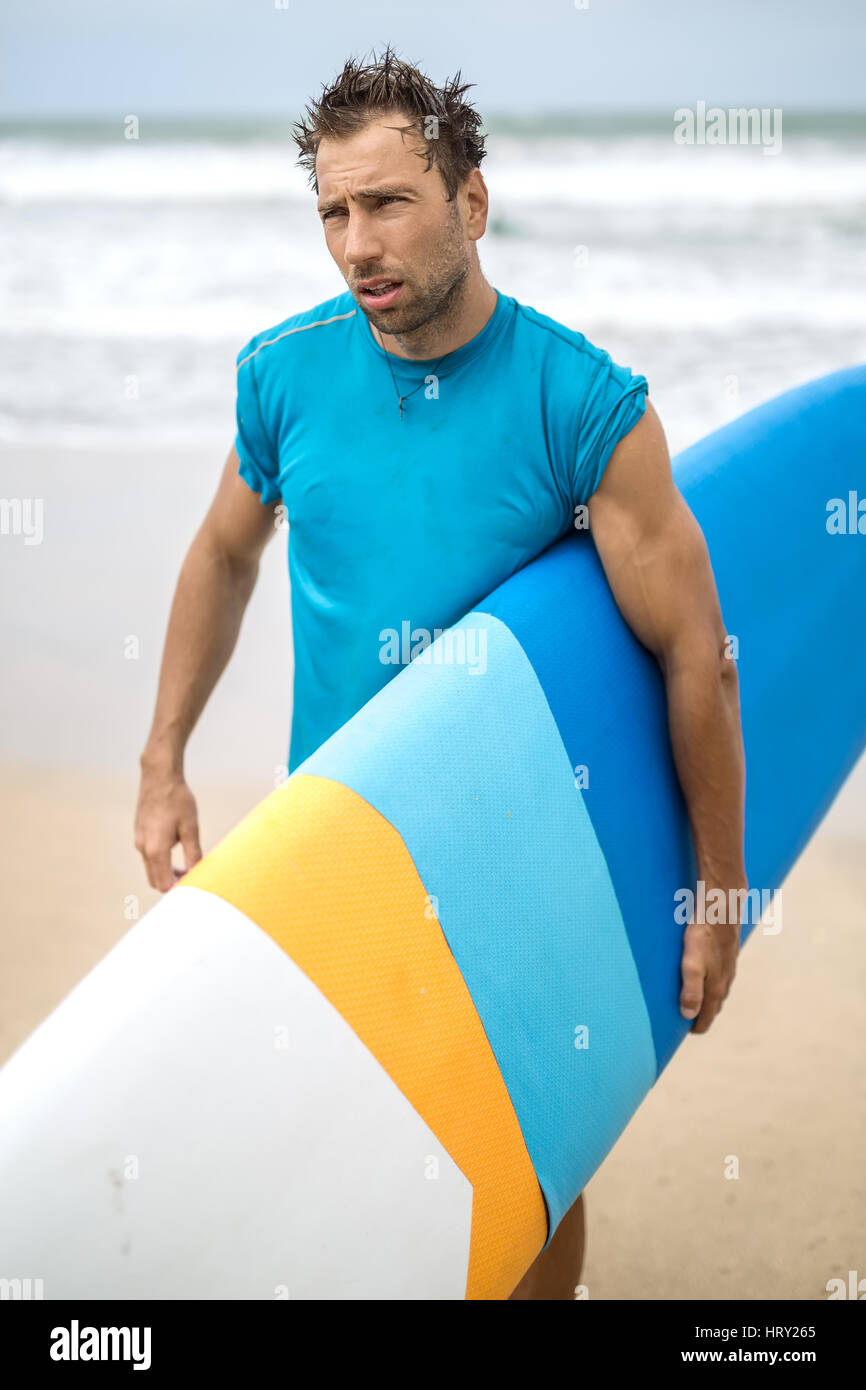 Guy strappalacrime con i capelli disheveled e la stoppia sorge sulla spiaggia sulla sfondo sfocato di le onde del mare e del cielo. Egli indossa una ciano Foto Stock