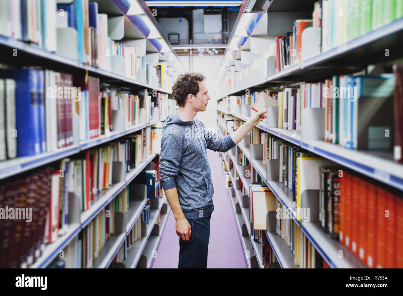 Studente nella biblioteca dell Università, giovane uomo caucasico tenendo prenota da scaffale, il concetto di istruzione Foto Stock