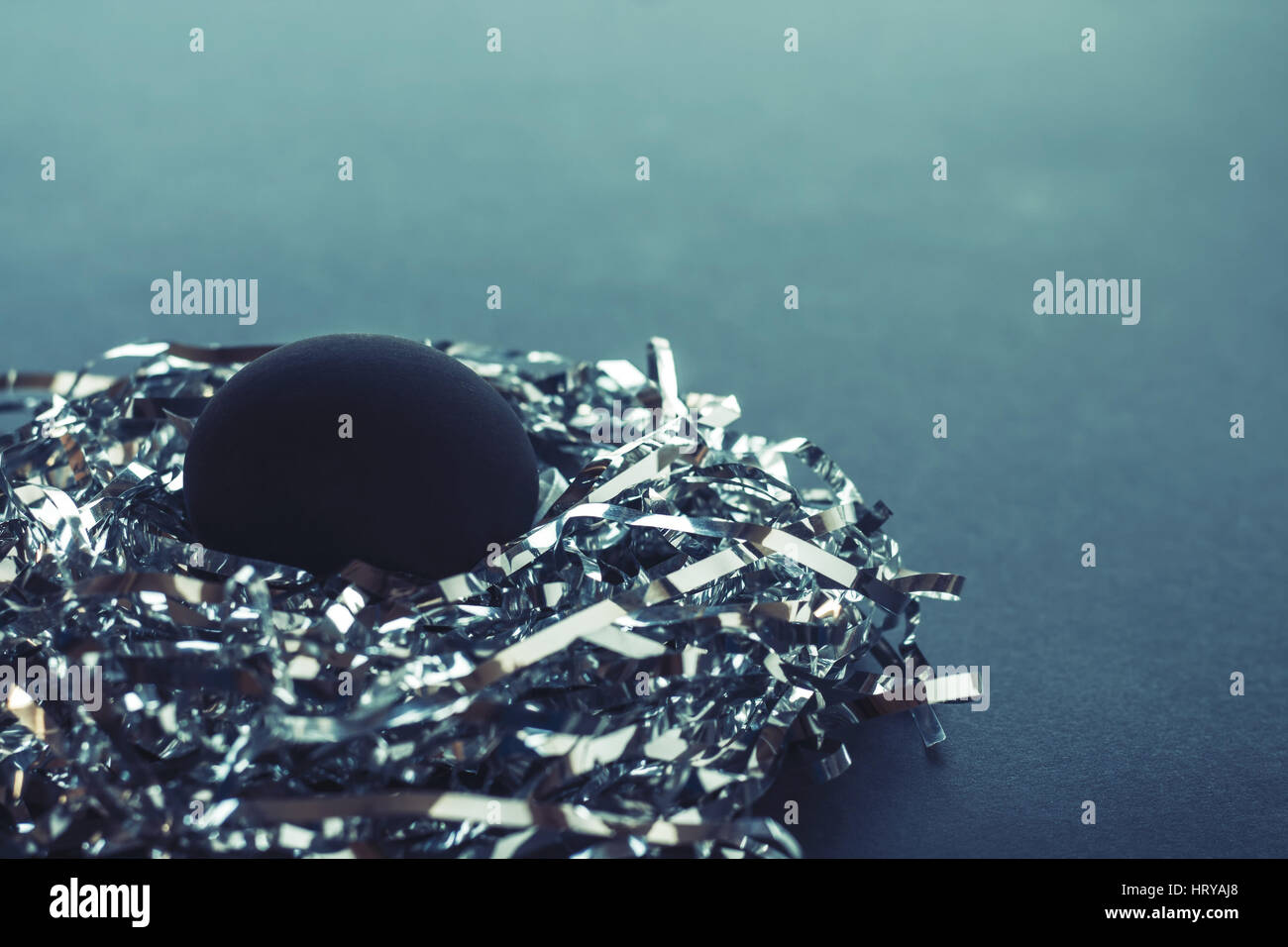 Un uovo nero in un nido fatto di stringhe di argento, su un verde blu sullo sfondo, concetto di Pasqua Foto Stock
