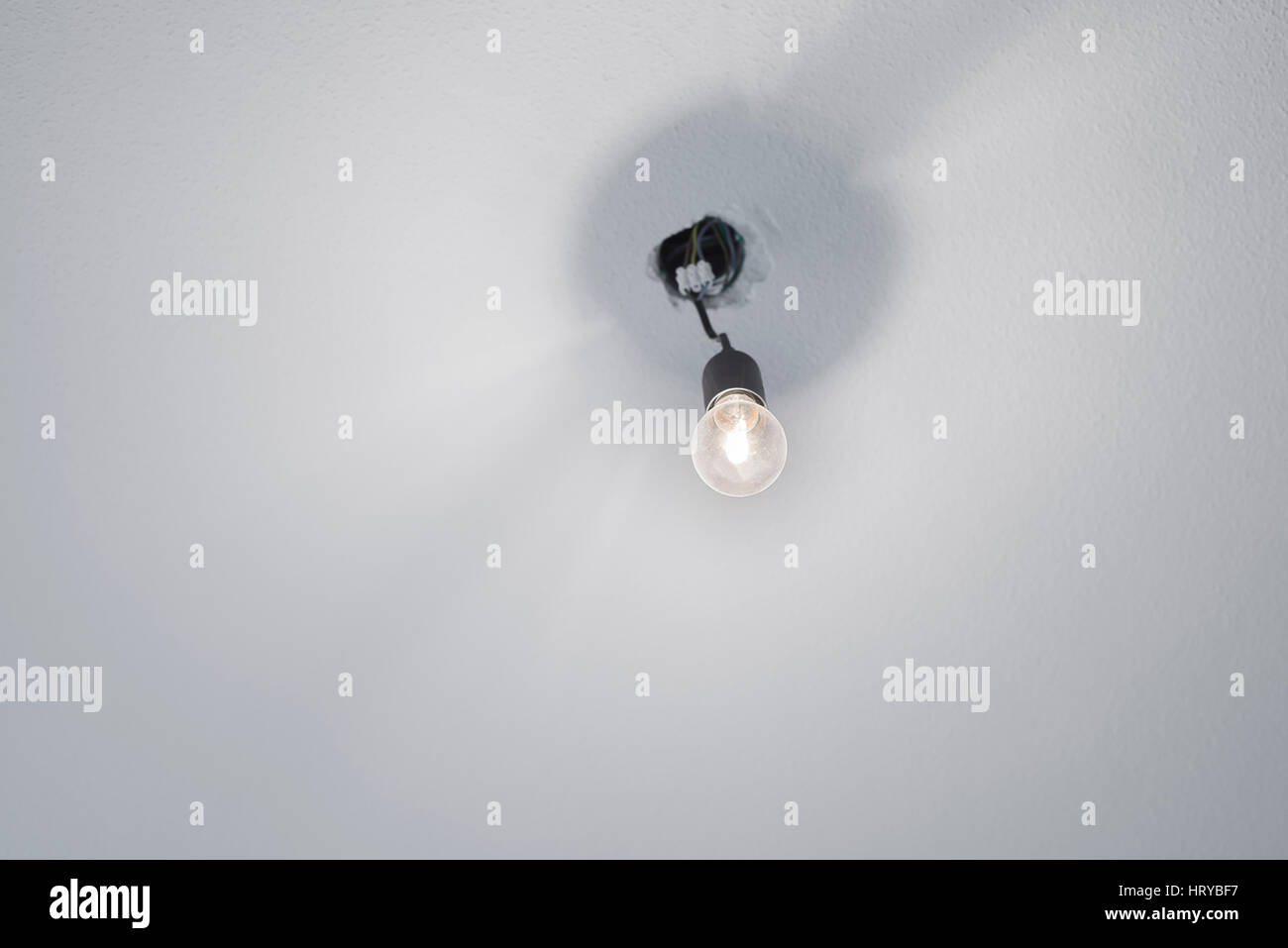 Illuminata alogeno lampadina incandescente in plastica nero portalampada presa con cavi di alimentazione sporgente da un soffitto con il bianco intonaco grezzo Foto Stock