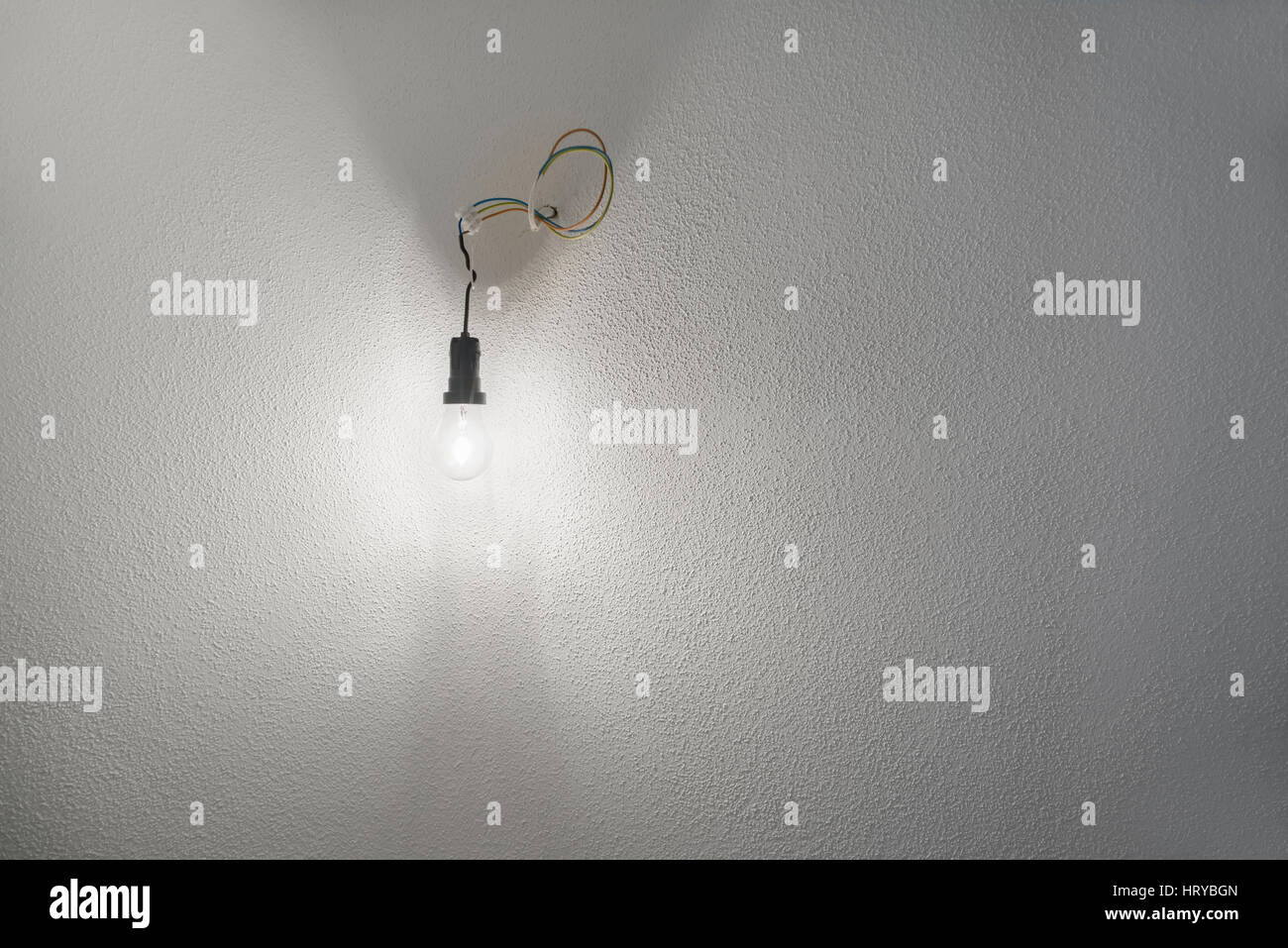 Illuminata alogeno lampadina incandescente in plastica nero portalampada presa con cavi di alimentazione sporgente da una parete con il bianco intonaco grezzo Foto Stock