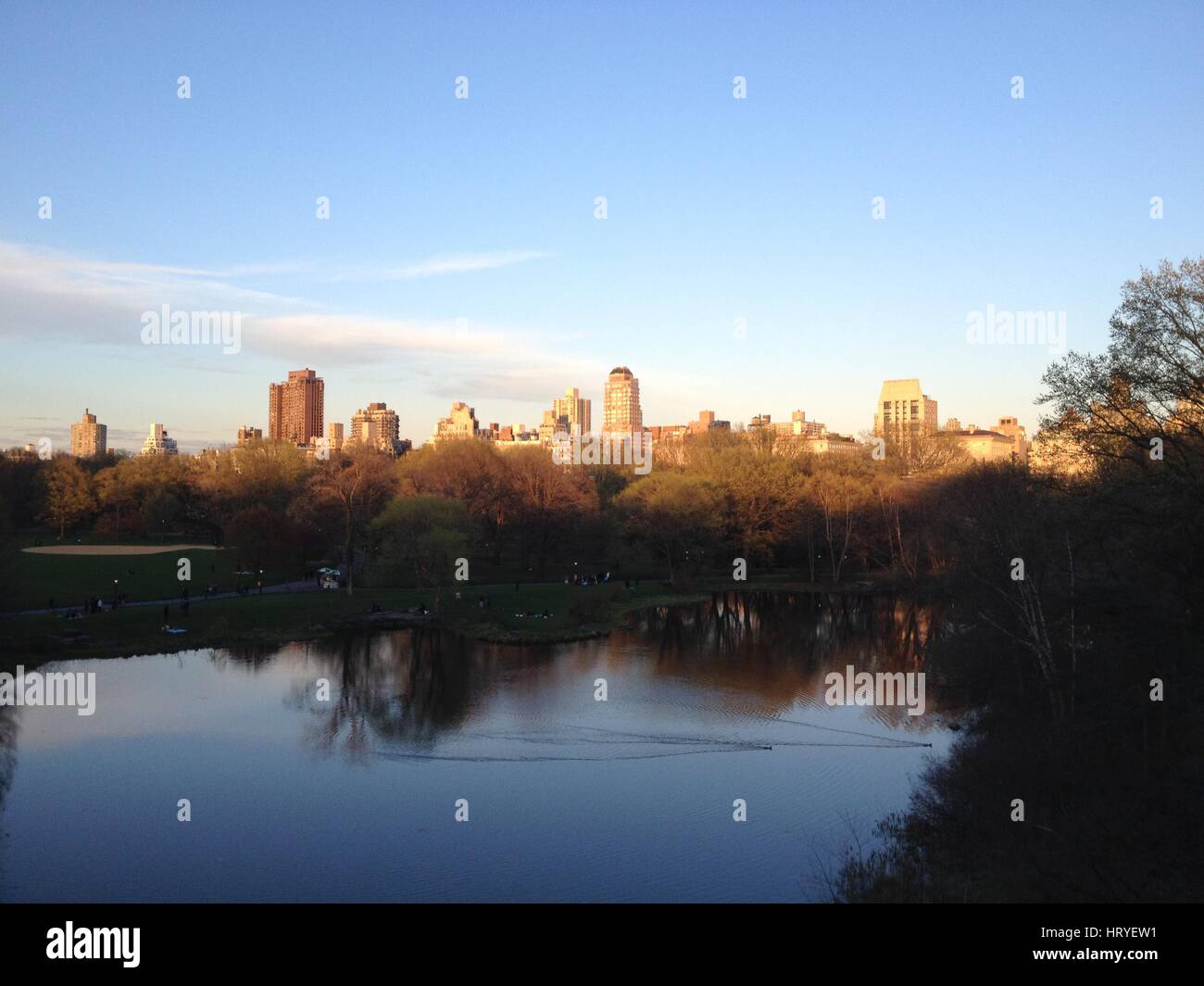 Central Park di New York. Sun impostazione sul lato est superiore, la riflessione di alberi e nuvole nel lago. Iconico Central Park al tramonto in New York. Foto Stock
