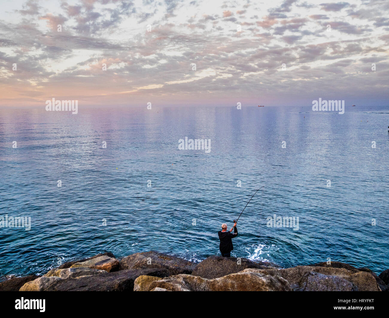 Uomo in piedi sul bordo delle rocce la pesca in mare, Staithes, North Yorkshire, Regno Unito. Foto Stock