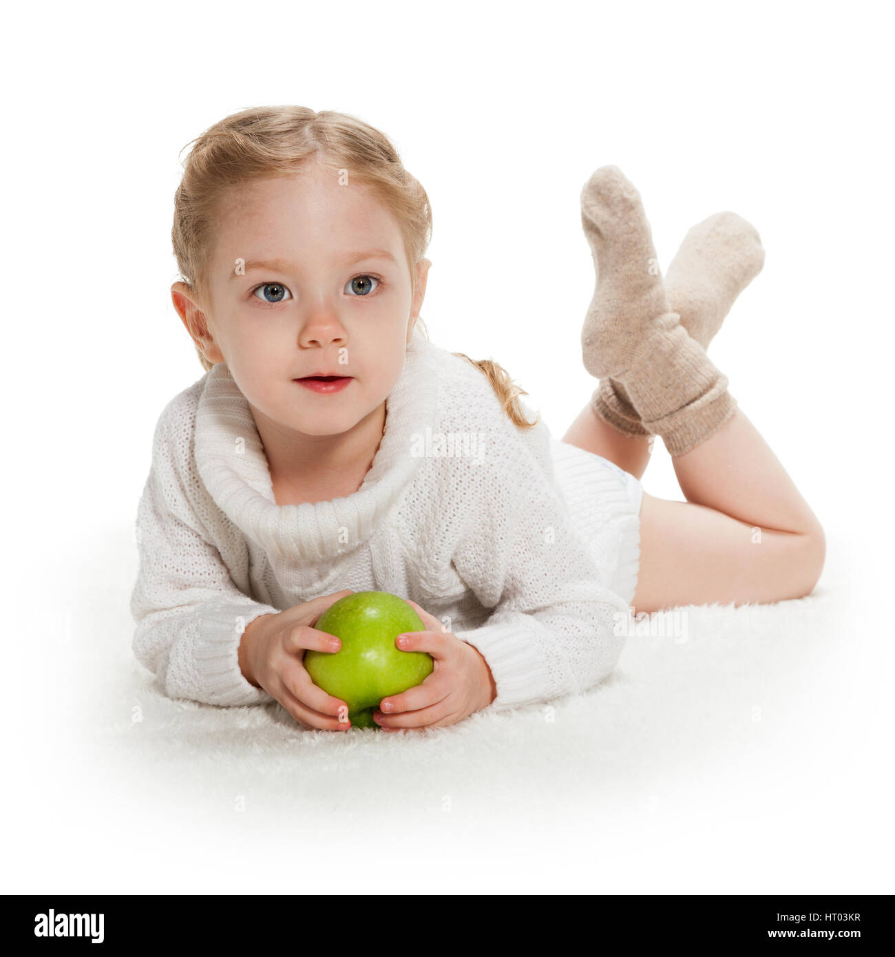 Tre-anno vecchia ragazza con mela verde fissa sul bianco tappeto lussureggiante Foto Stock
