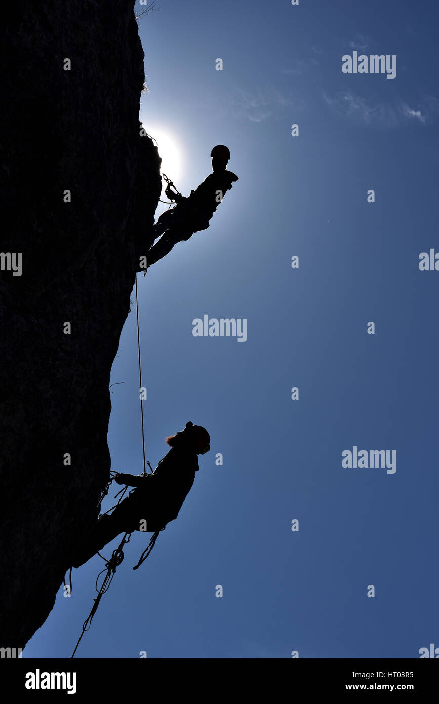 Silhouette di hanging rock arrampicatori su una parete Foto Stock