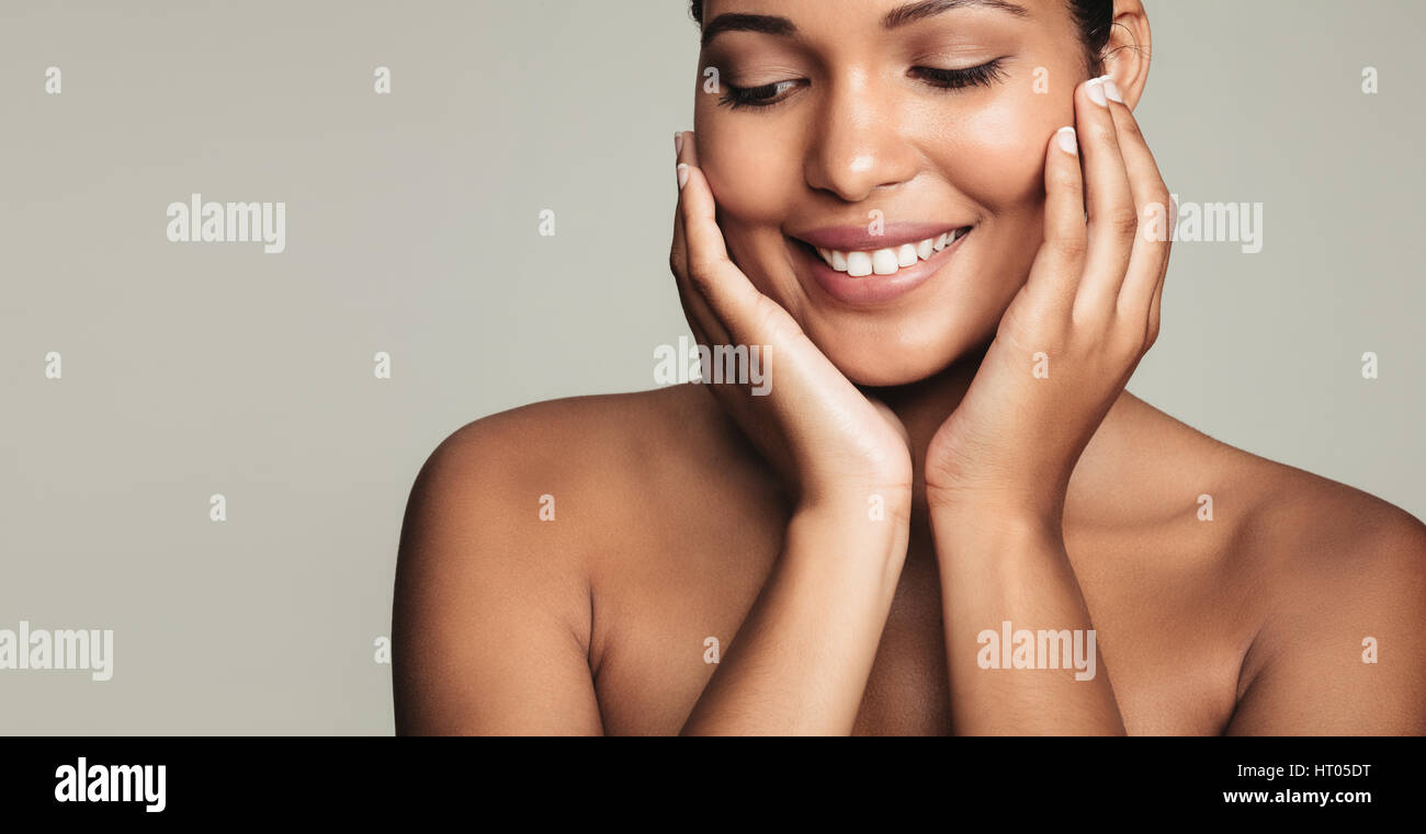 Primo piano della sorridente giovane donna con pulito e pelle sana su sfondo grigio. Bella femmina modello toccando il suo volto. Foto Stock