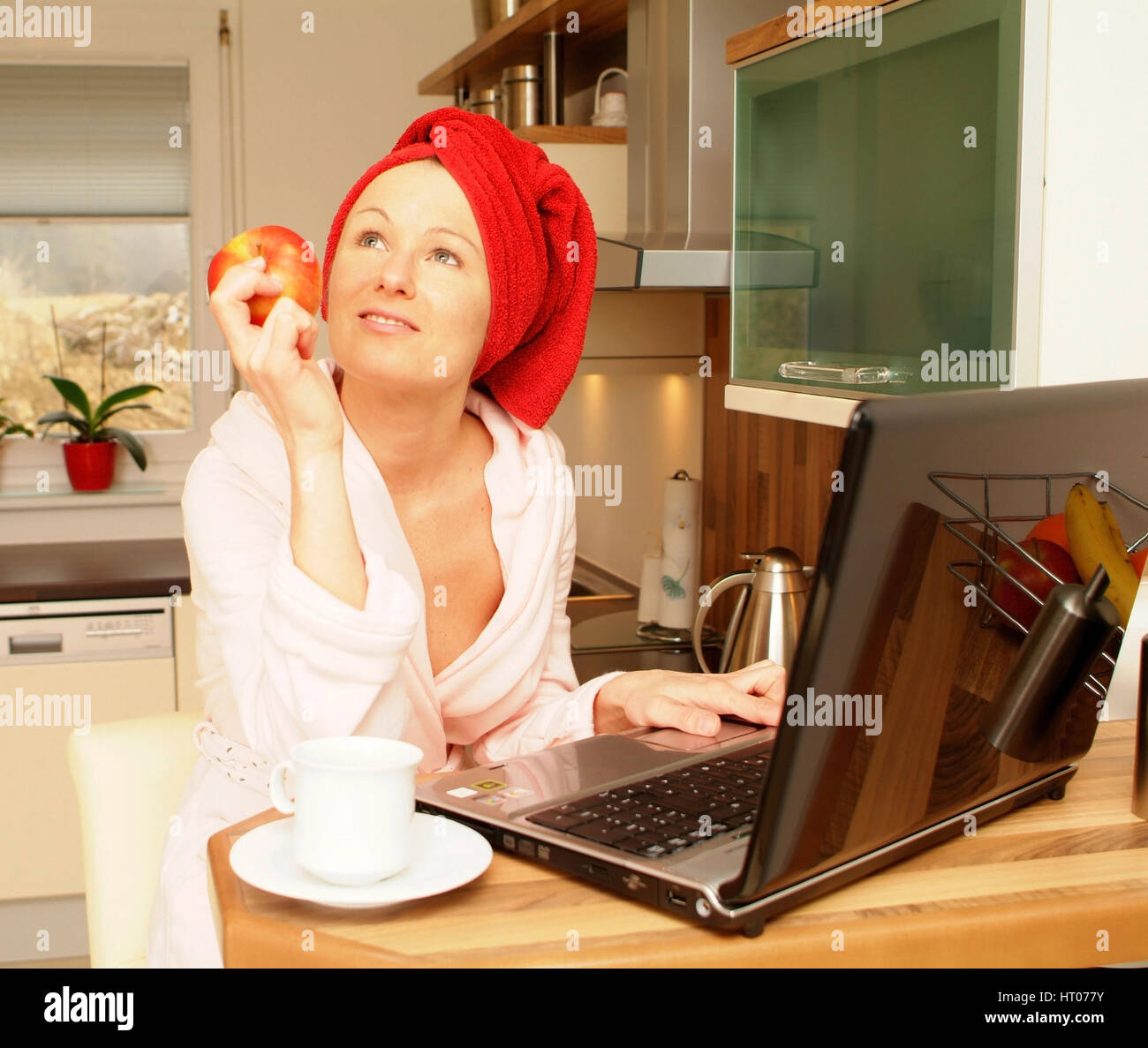 Junge Frau im Morgenmantel arbeitet am Notebook und isst einen Apfel - giovane donna in accappatoio utilizzando laptop e mangiare un Apple Foto Stock