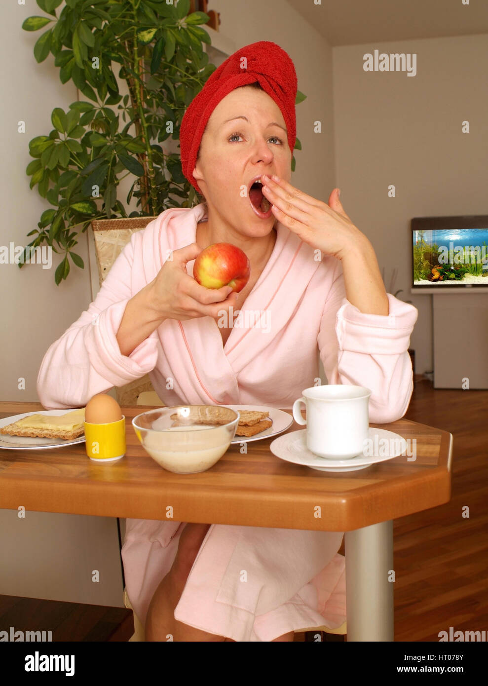 Junge Frau im Morgenmantel sitzt beim Fruehstueck und gaehnt - giovane donna in accappatoio schiusi a colazione Foto Stock