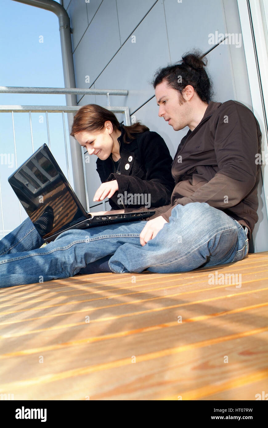 Junges Paar sitzt Notebook mit am sonnigen alkon - coppia giovane sul balcone utilizzando laptop Foto Stock