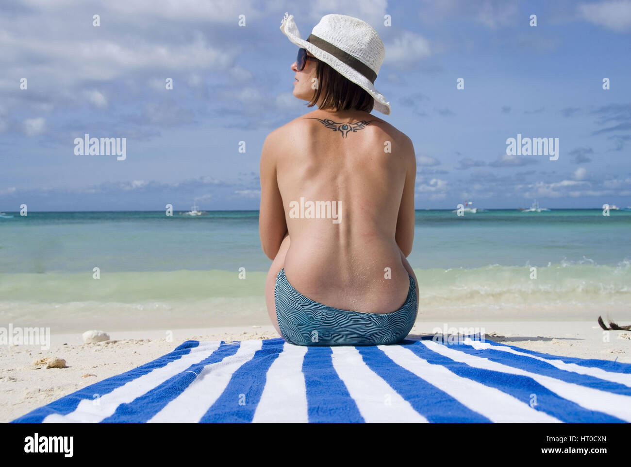 Junge Frau sitzt oben ohne am Strand - donna sulla spiaggia Foto Stock