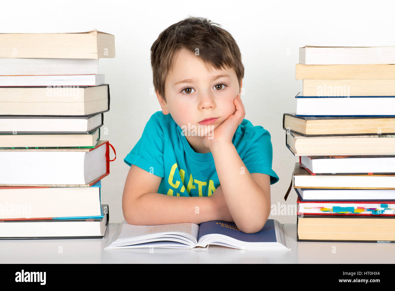 Annoiato ragazzo seduto tra la pila di libri. Isolato su uno sfondo bianco. Foto Stock