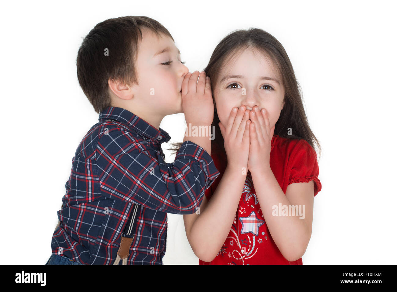 Little Boy whispering storia divertente in una ragazza in un orecchio. Lei è sempre sorridente e che copre la bocca con le mani. Isolato su uno sfondo bianco. Foto Stock