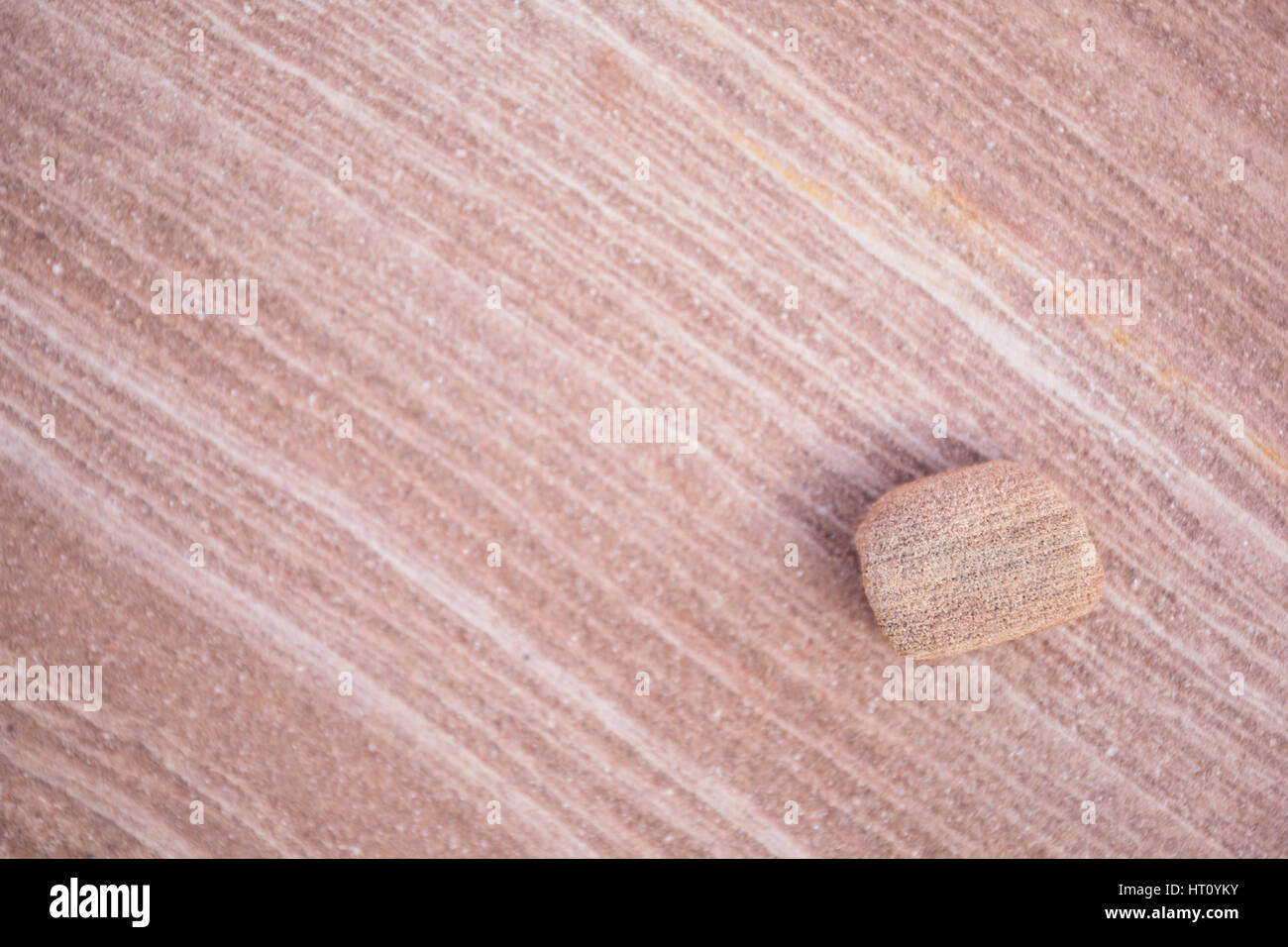 Una piccola roccia arenaria in appoggio su una grande lastra di più livelli di colore rosa e bianco rock. Profondità di campo lascia la piccola roccia nella messa a fuoco e il backgroun Foto Stock