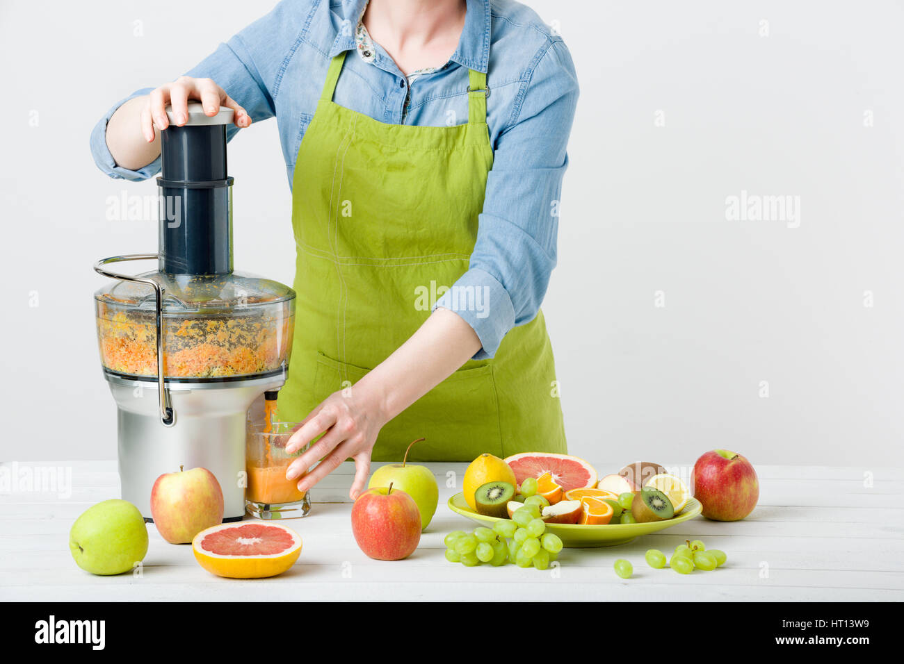 Anonimo donna che indossa un grembiule, la preparazione di un sano succo di frutta utilizzando moderne spremiagrumi elettrico, uno stile di vita sano concetto su sfondo bianco Foto Stock